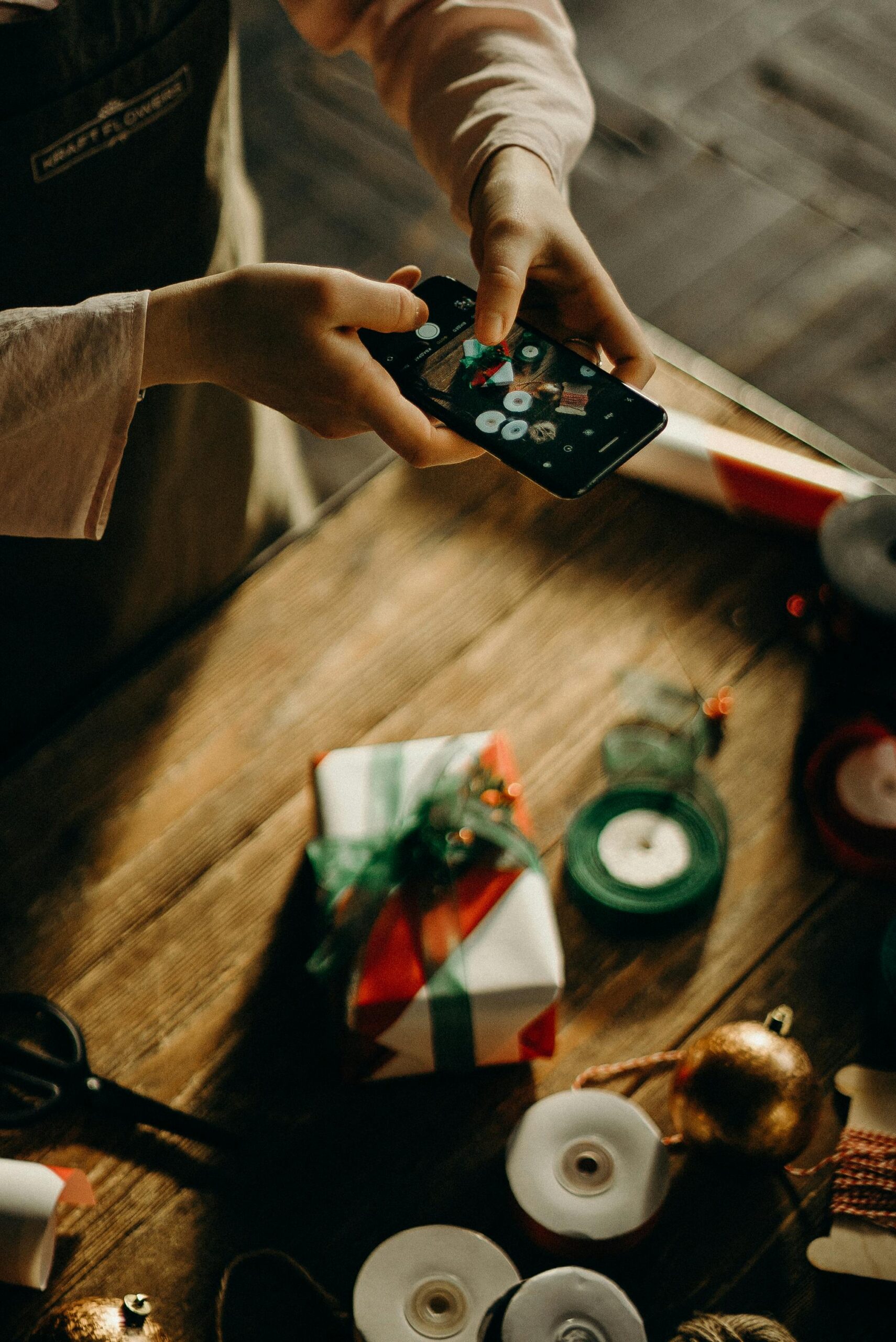 Hands taking a picture of a wrapped Christmas present with a phone.