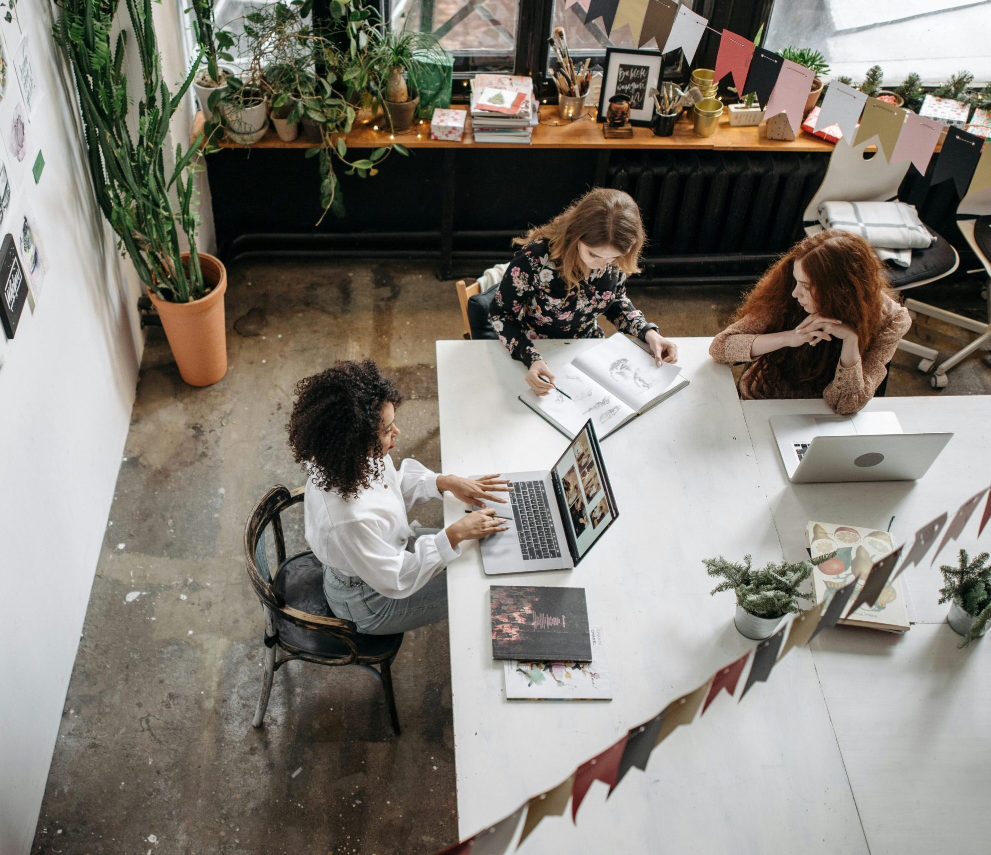 A team of women collaborates around laptops and notes in an office.